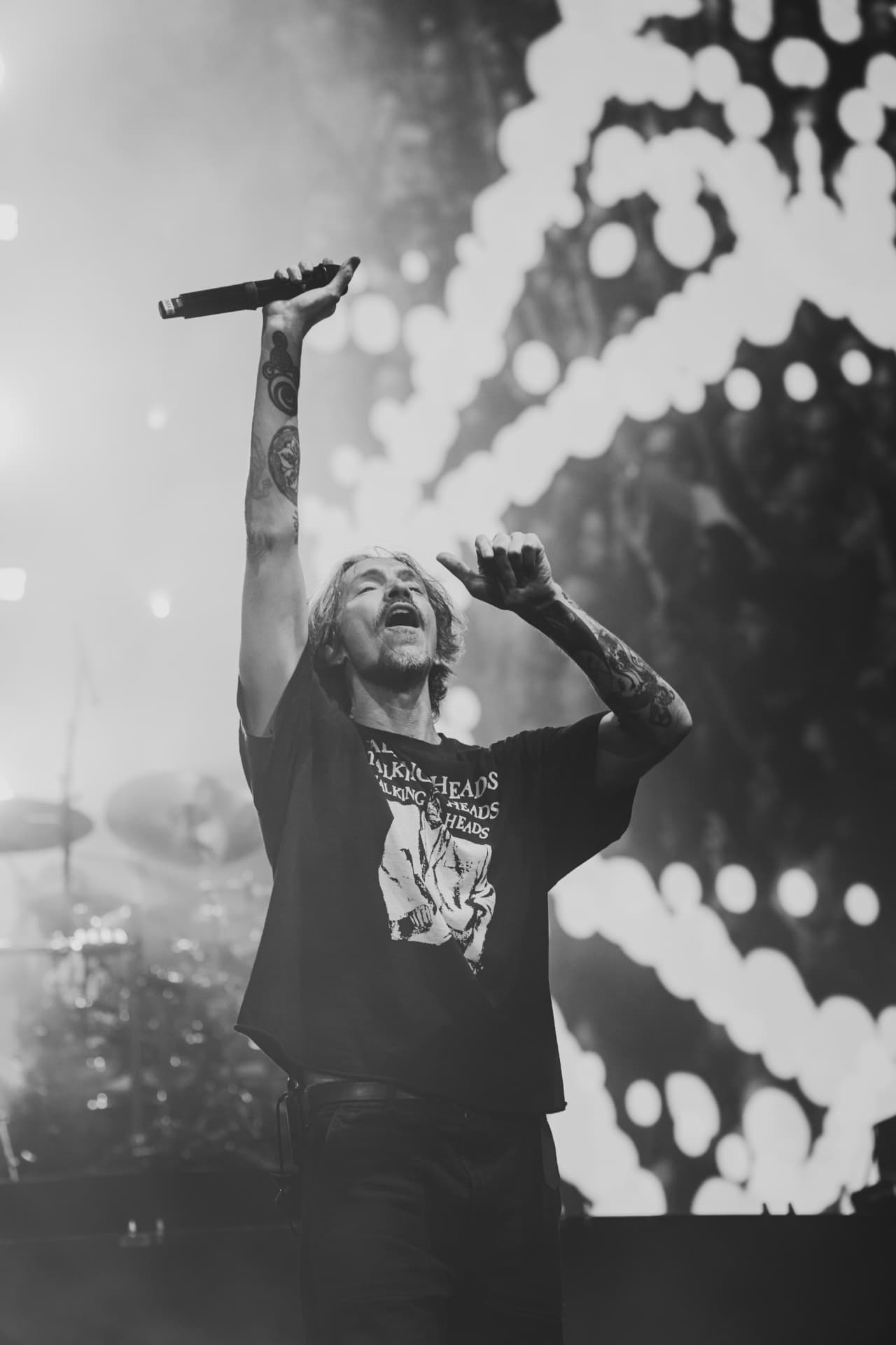 Black-and-white shot of the singer with one tattooed arm raised holding the microphone high