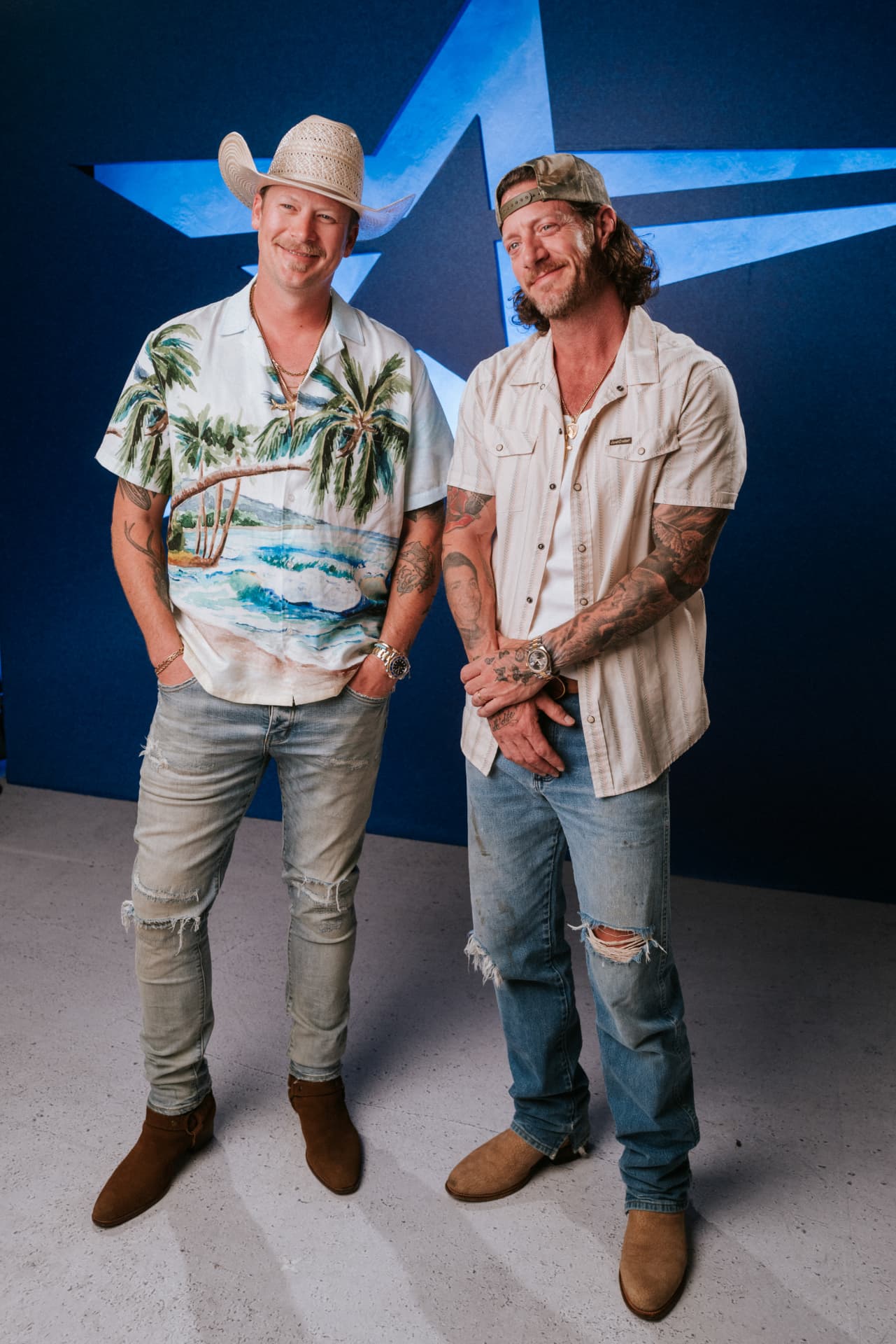 The two artists posing full length together against a blue wall with a large backlit star cutout behind them