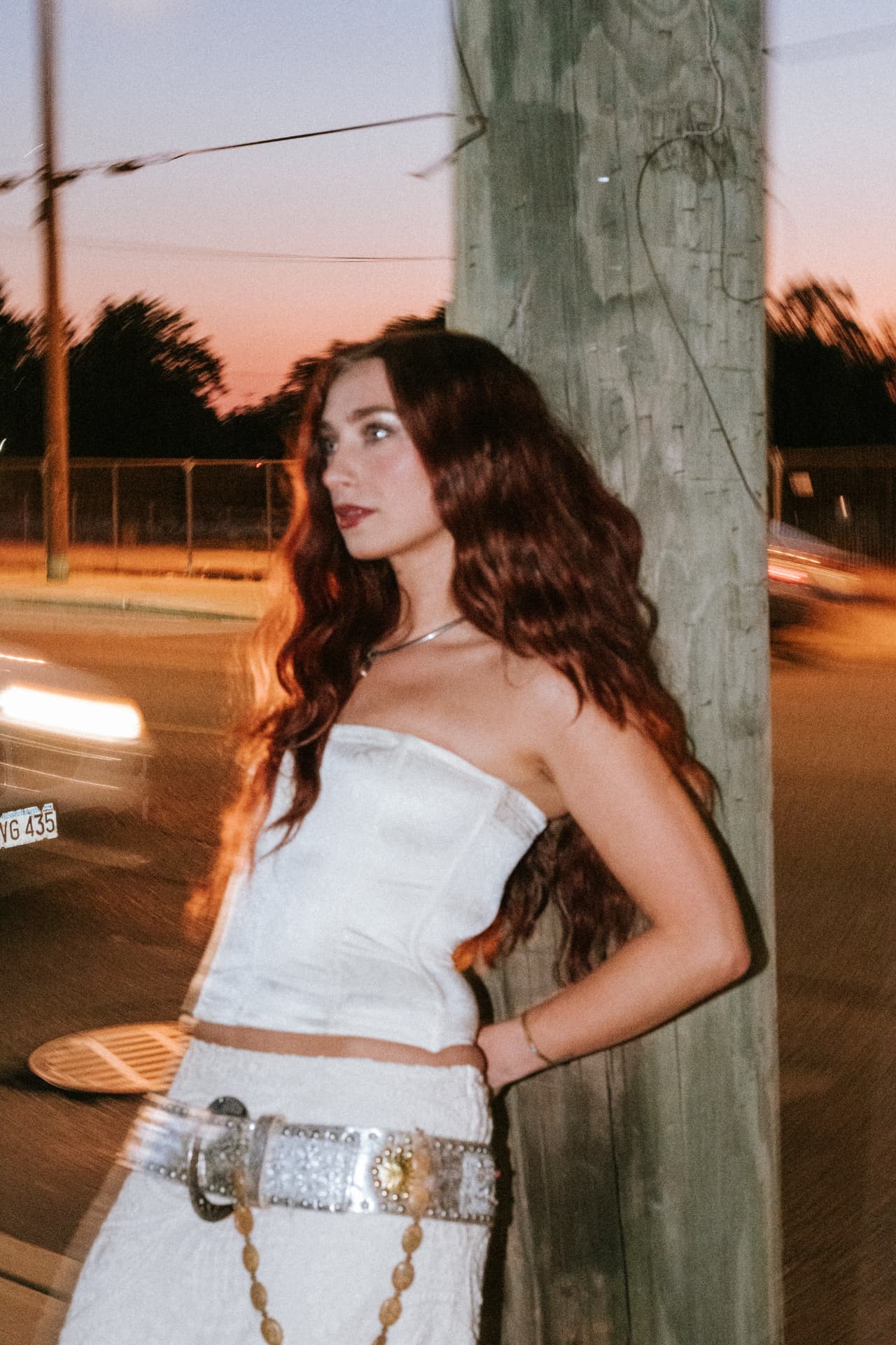 Anna Graves in a white strapless outfit against a telephone pole at dusk