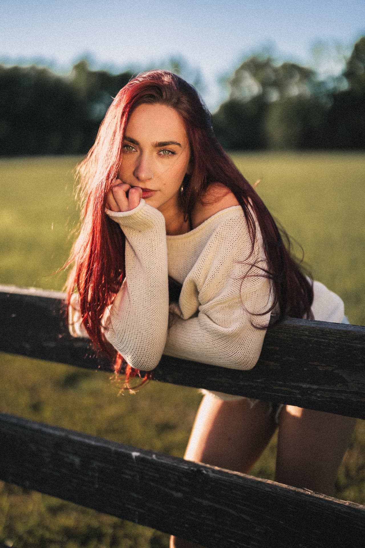 Anna Graves leaning on a wooden fence in a field at golden hour