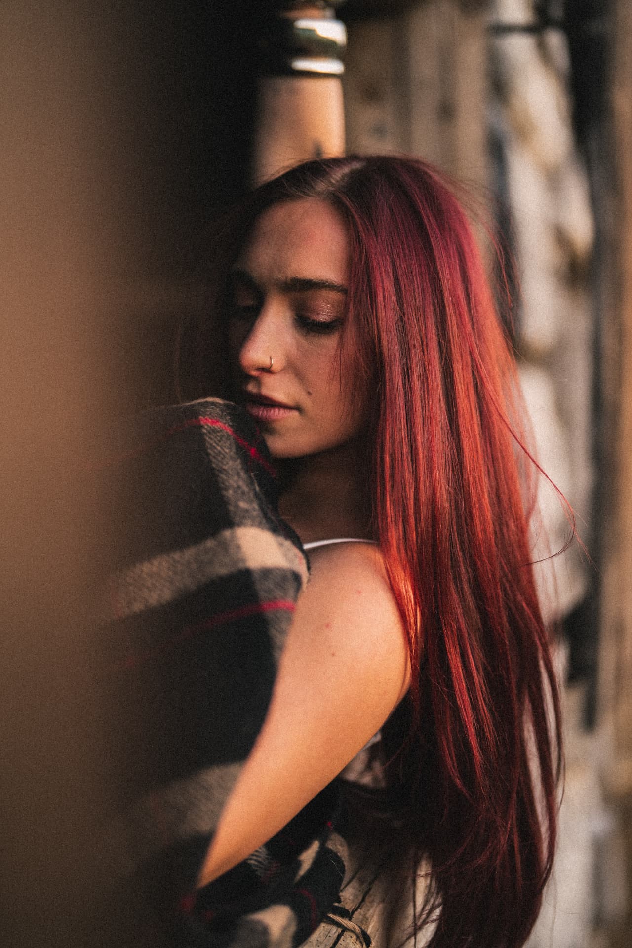 Anna Graves with her long red hair over her shoulder, eyes closed, resting her cheek against a plaid blanket