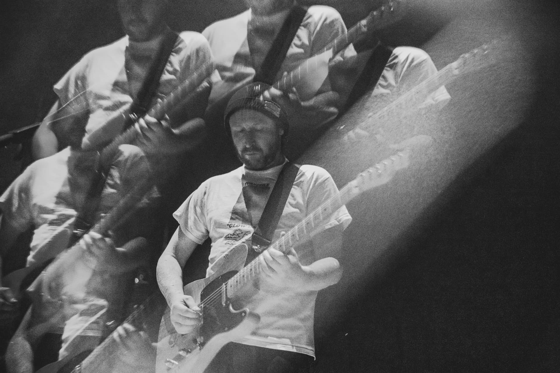 Black-and-white double exposure of a guitarist in a beanie playing, layered with ghosted motion trails