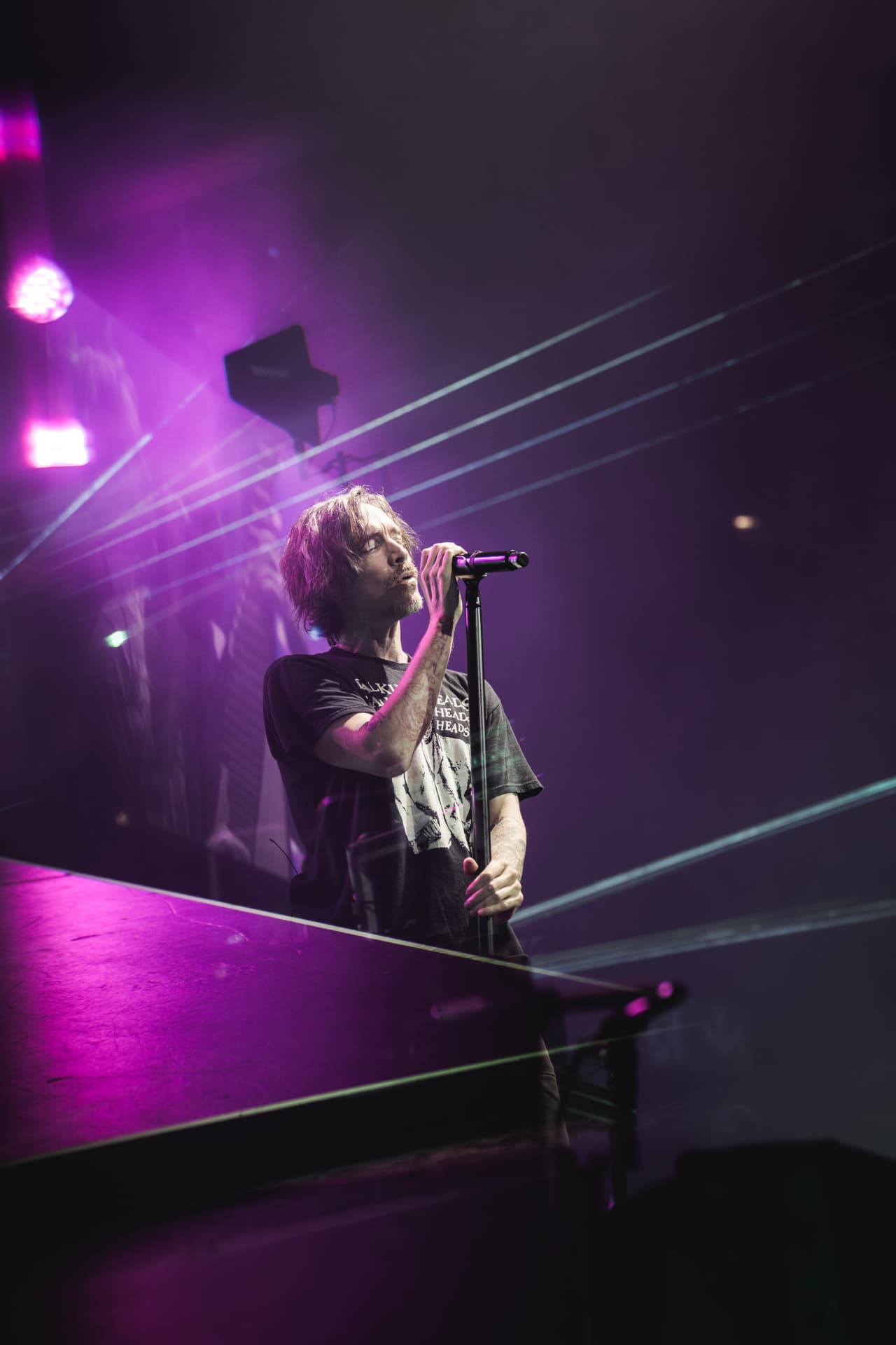 The singer leaning on a mic stand under magenta laser light with beams cutting across the frame