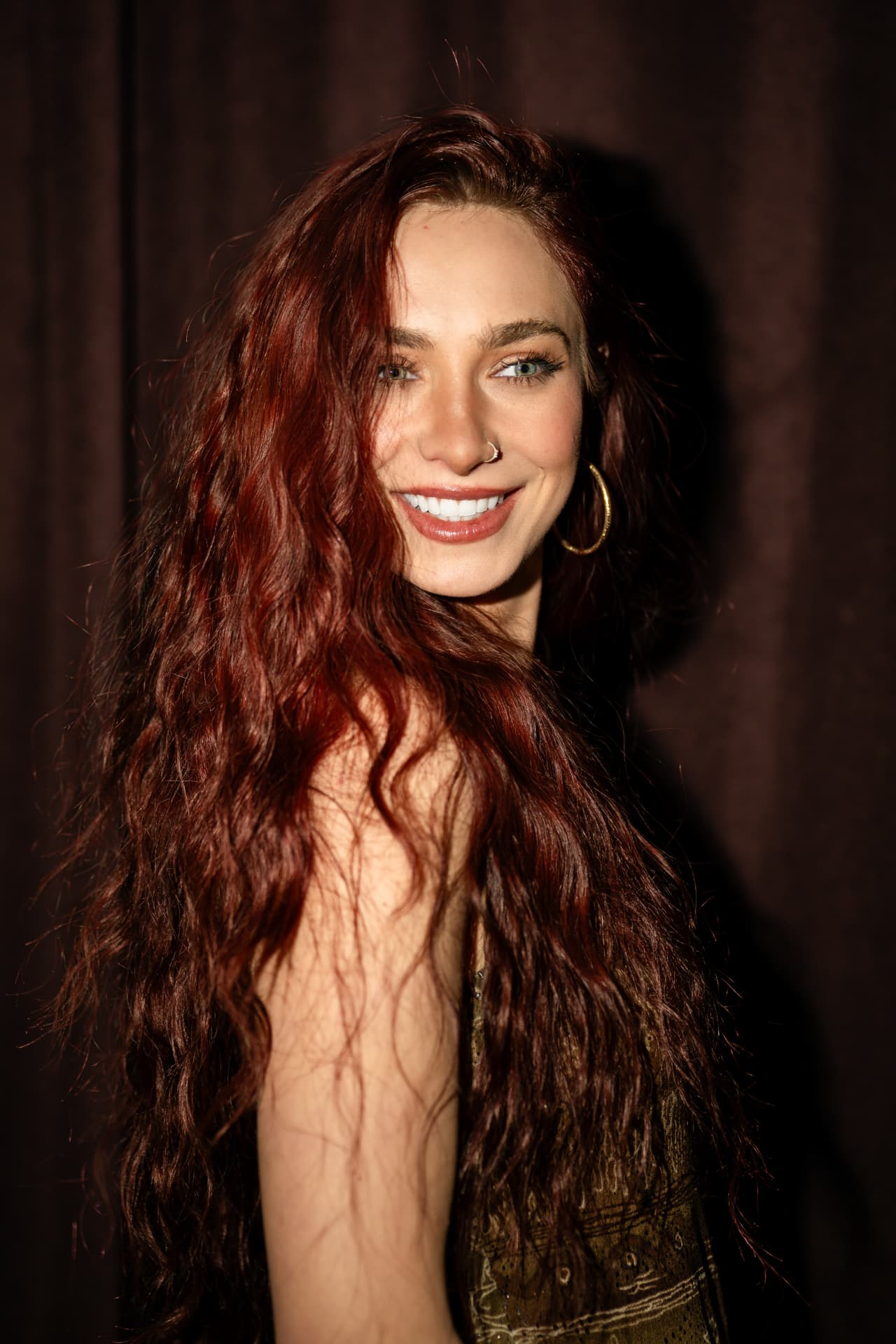 Anna Graves smiling over her shoulder against a dark curtain