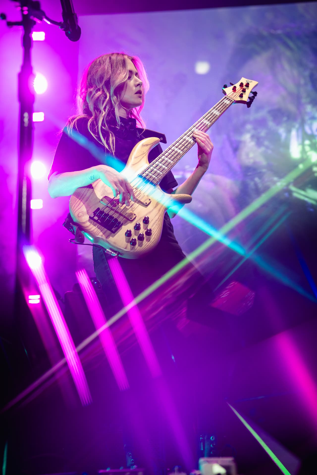 The bass player playing a natural-wood bass under purple and pink light with a green laser streak across the frame