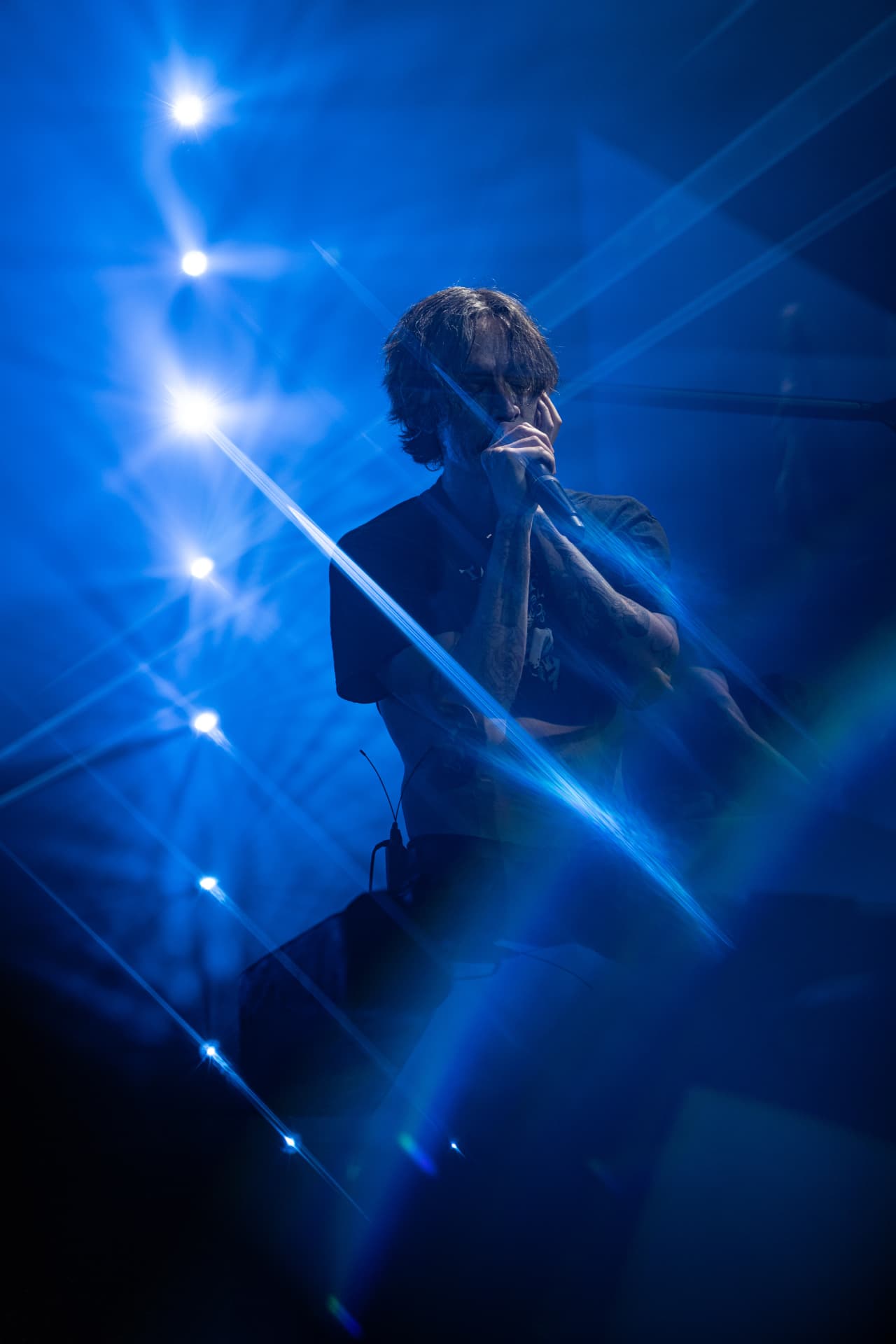 The singer gripping the microphone amid blue laser beams and stage lights