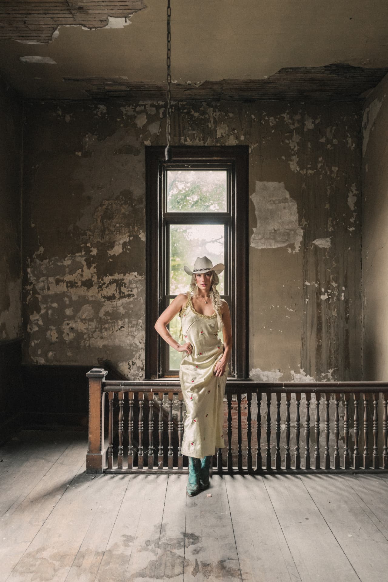 Diner standing full length in front of a tall window inside a rustic room with peeling walls and an exposed ceiling
